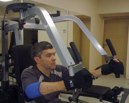Hombre entrenando en máquina de rehabilitación con agarres adaptativos Active Hands. Neurorrehabilitación de la mano. Garra Adaptive Argentina.